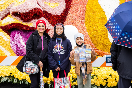 Three females smile in front of elaborate Rose Parade float