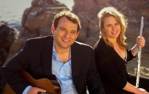 two smiling instrumentalists on a sunny hillside with rocks behind