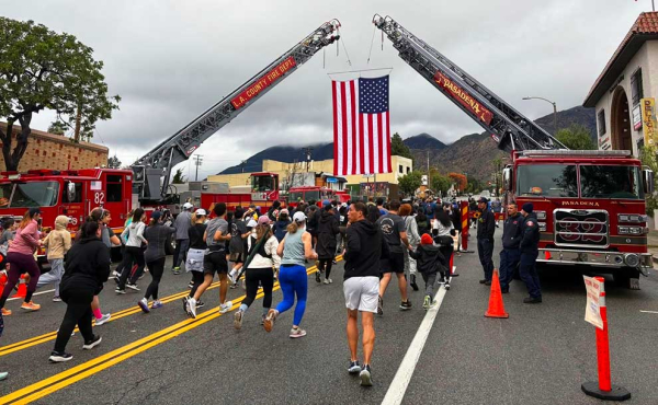 runners under a flag held by two fire trucks