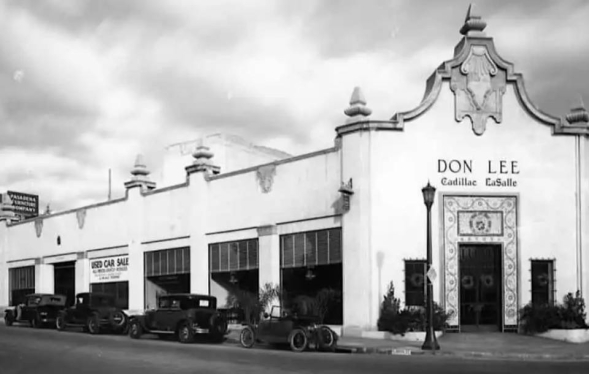 black and white Spanish fantasy style building with car dealership inside and 1920s era vehicles parked out front