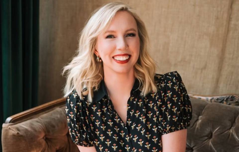 blond woman with black blouse on a green chaise smiles