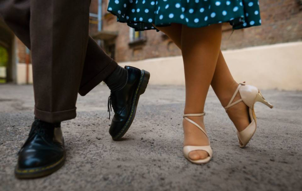 Photo of man's legs in trousers and dancing shoes next to woman's polka dot skirt and white dancing heels