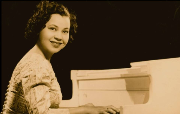 black and white photo of African American woman smiling and playing a white piano