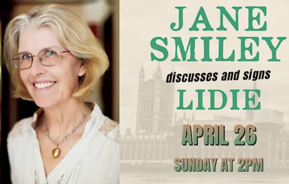 White woman with white-blond hair and golden eyeglasses smiles with banner about book signing