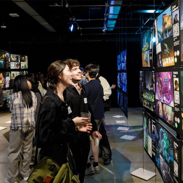 two college-aged adults smile up at backlit art displays down a long dark corridor lit by commercial art