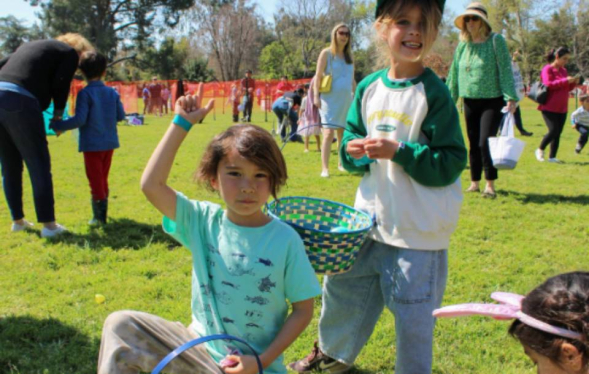 kids holding Easter eggs above head with a basket in a busy public park