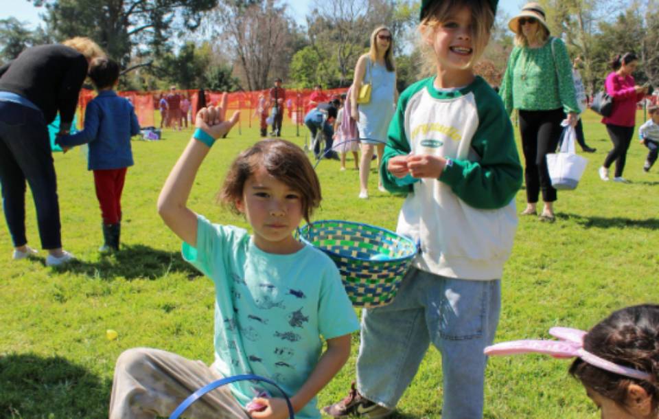 kids holding Easter eggs above head with a basket in a busy public park